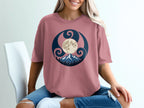 Pink t-shirt with circular moon, mountain, and forest graphic design.
