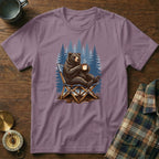 Bear sitting in a chair, holding a mug, with a forest background.