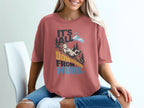 A woman sits wearing a dusty rose t-shirt featuring a cartoon goat sliding down a mountain with the text It's All Downhill From Here.