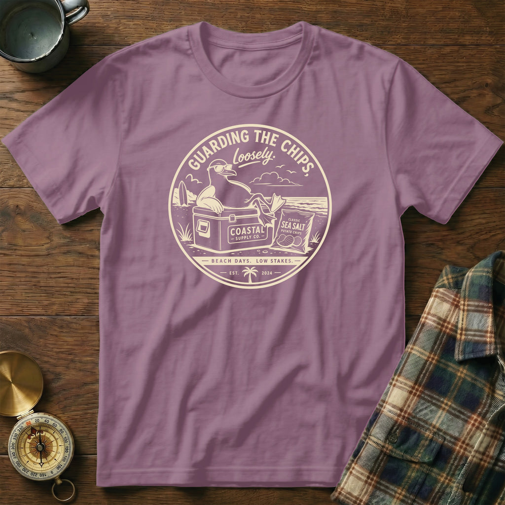 A purple t-shirt featuring a circular graphic with a seagull wearing sunglasses on a cooler.