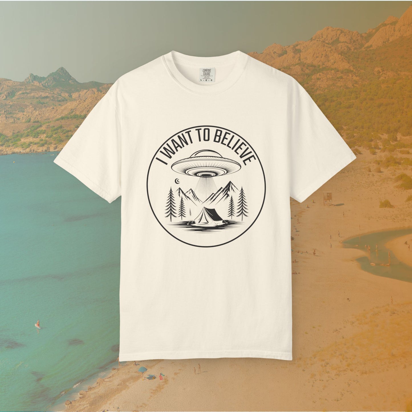 ivory  t-shirt A round, white graphic on a dark background featuring a classic flying saucer UFO abducting a tent at a campsite surrounded by mountains and pine trees. The surrounding text reads "I WANT TO BELIEVE.