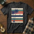Black t-shirt with vintage palm trees and sunset stripes graphic.