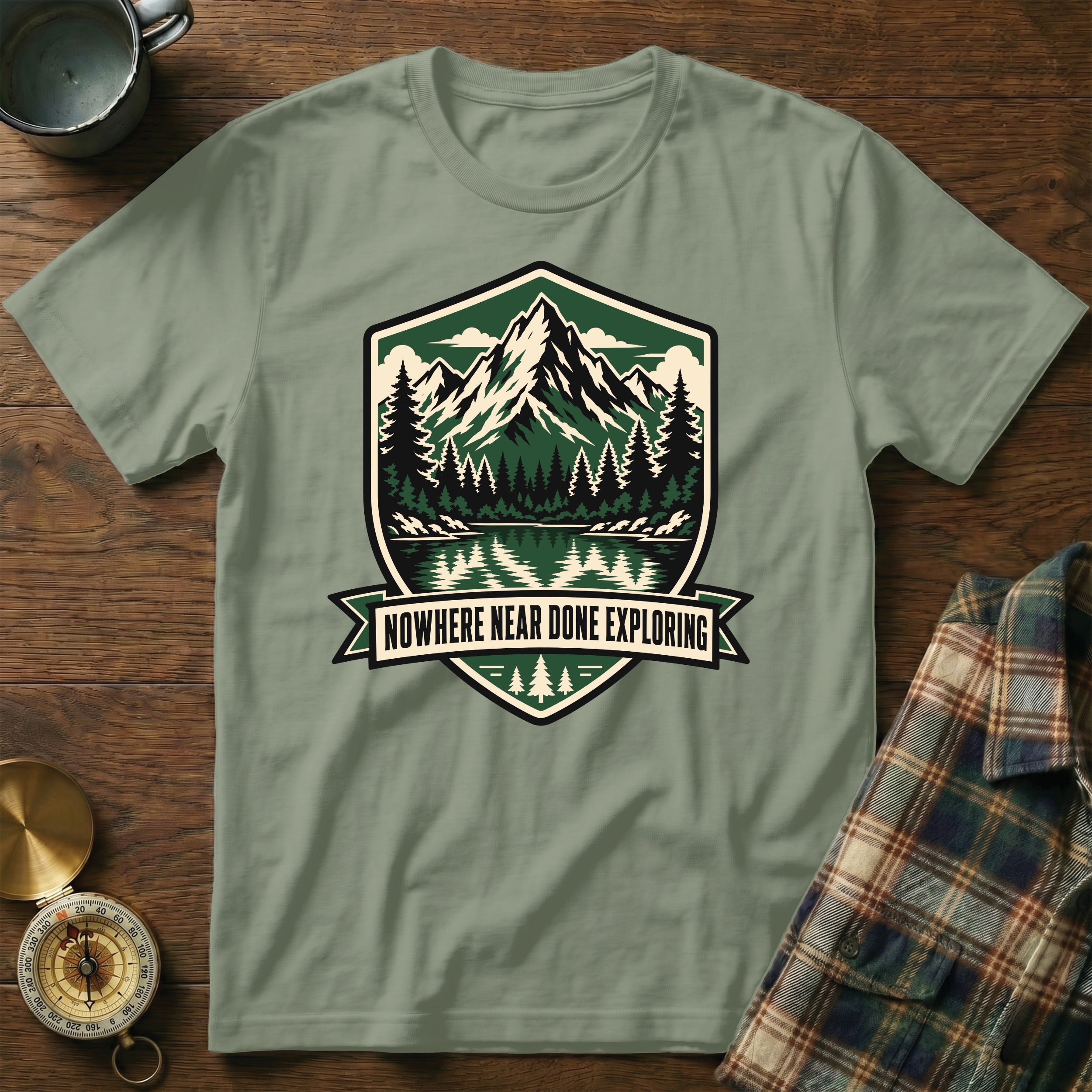 Green t-shirt with mountain lake graphic and "Nowhere Near Done Exploring" text.