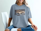 Light blue t-shirt with "ROUGHING IT." text and a beach scene graphic.