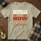 Beige t-shirt featuring the text REVEILLE IS NOW OPTIONAL EFFECTIVE IMMEDIATELY, laid flat on wooden surface.