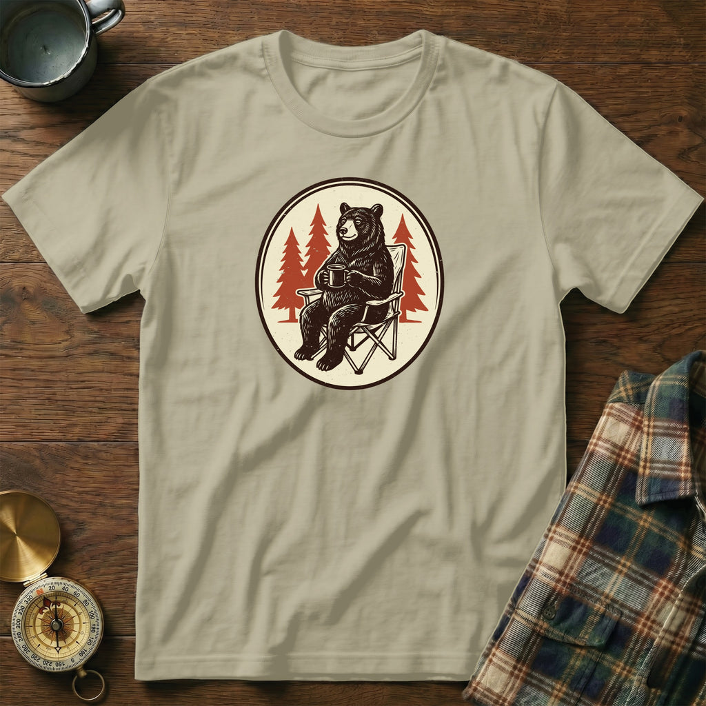 Bear in camp chair holding mug with pine trees in circle design on shirt.