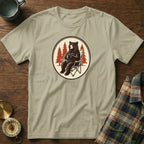 Bear in camp chair holding mug with pine trees in circle design on shirt.