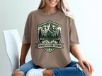 Brown t-shirt with mountain and lake graphic and text "Nowhere Near Done Exploring".