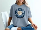 Grey t-shirt with circular moon, mountains, and trees graphic design.