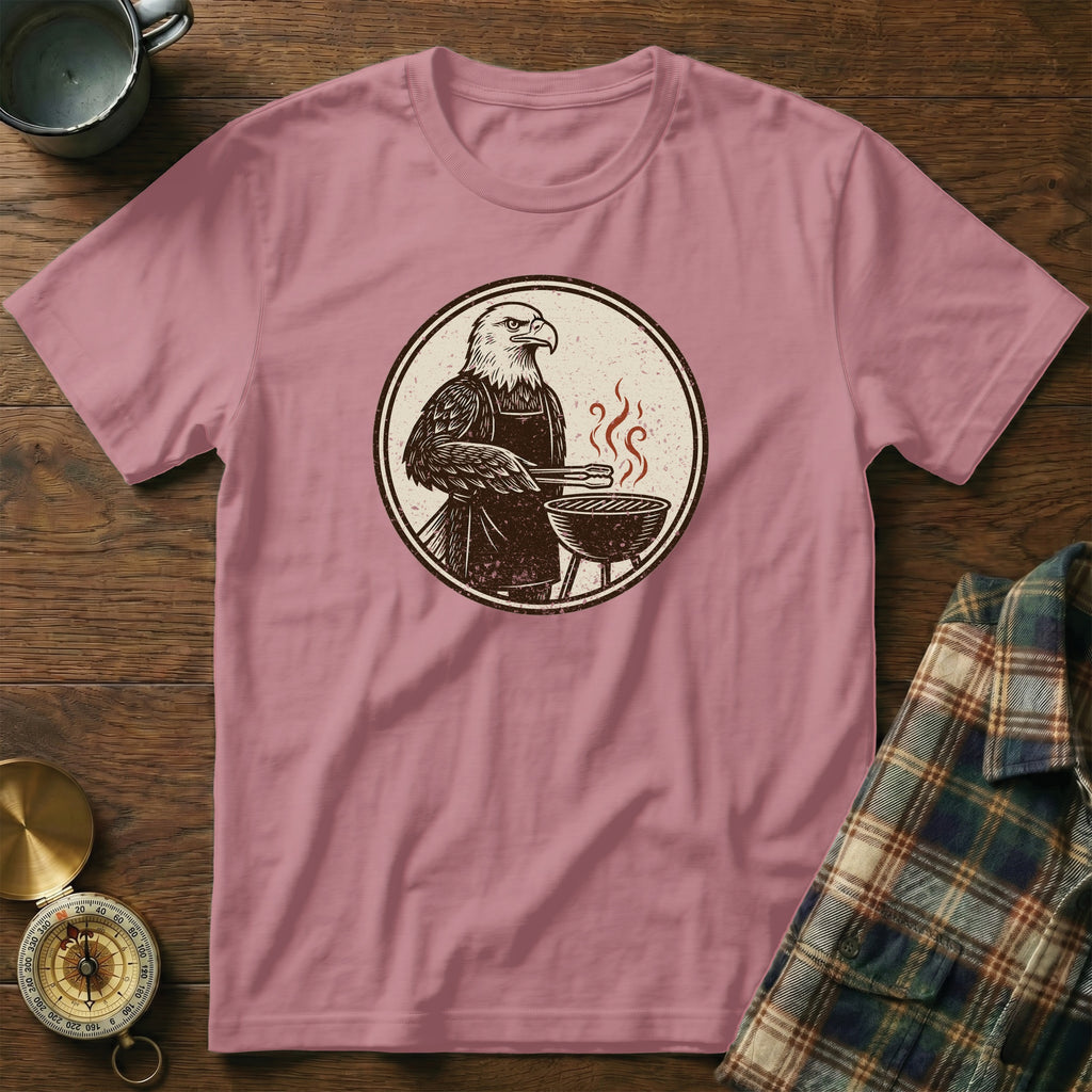 T-shirt with a graphic of an eagle wearing an apron grilling by a barbecue.