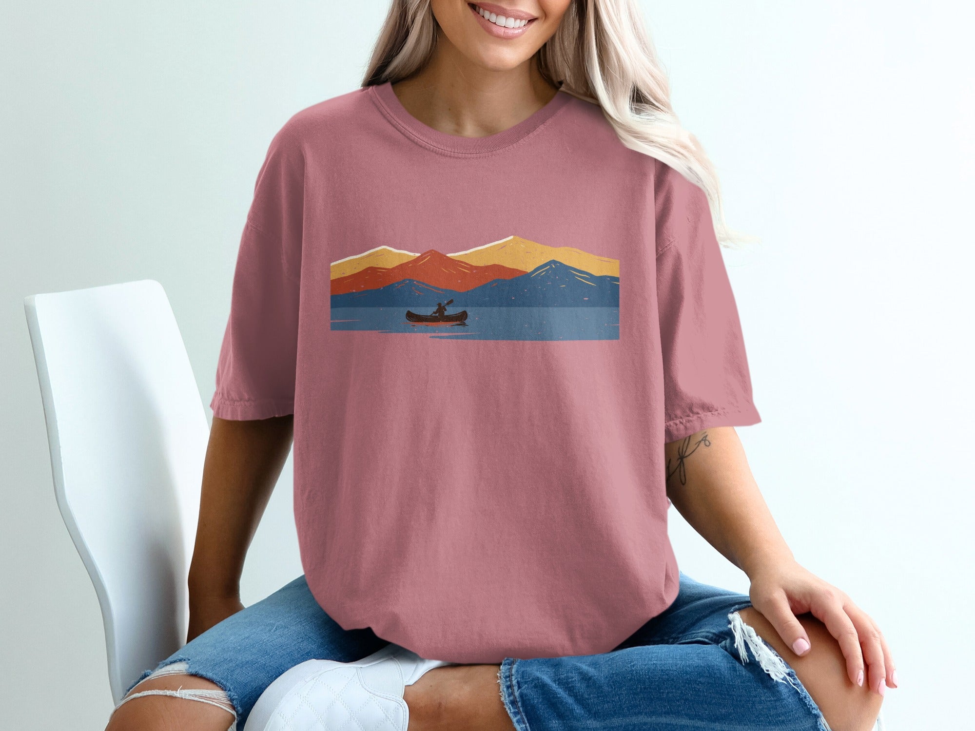 T-shirt graphic of a canoeist on a lake with colorful mountains in the background.
