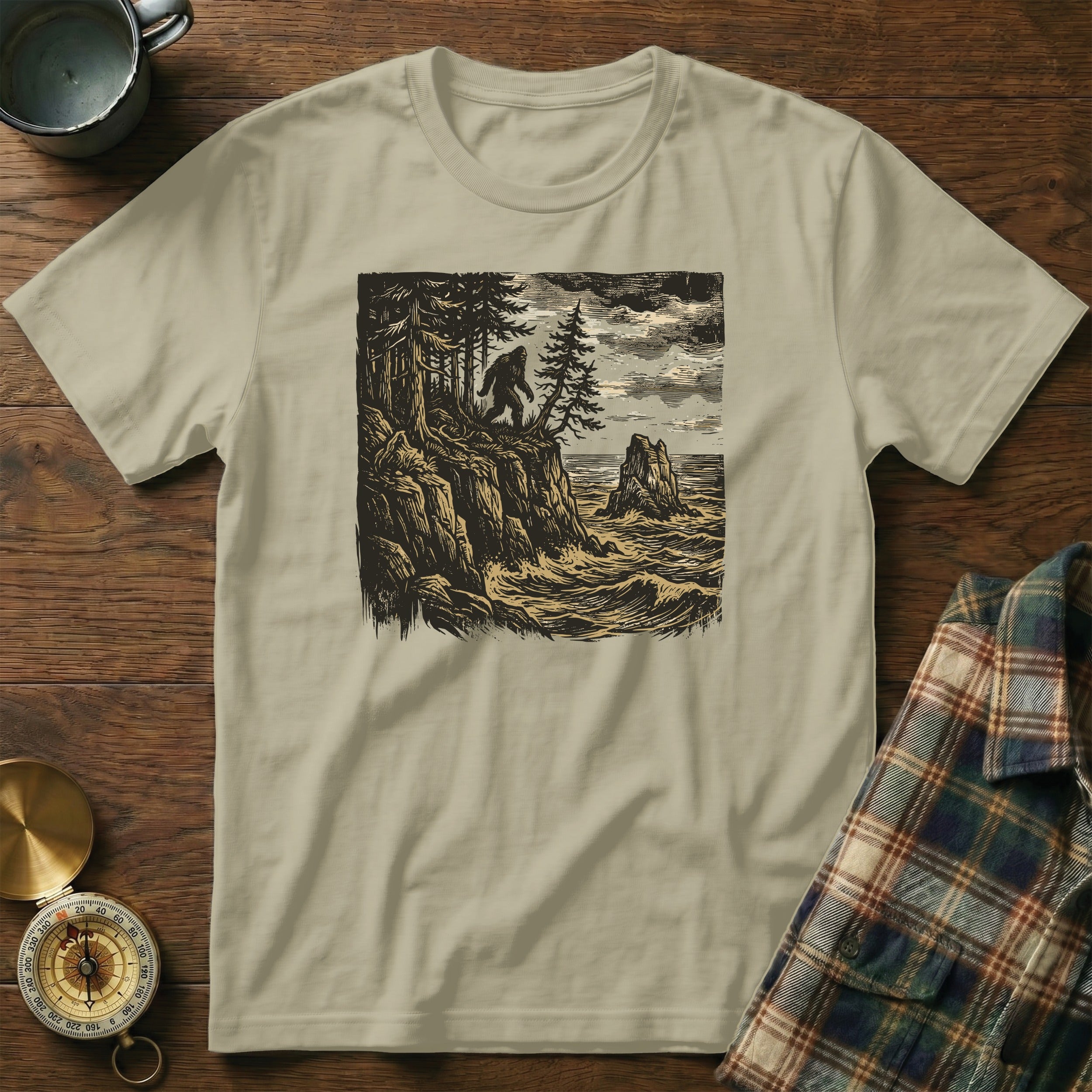 T-shirt with Bigfoot silhouette on cliff overlooking stormy ocean and rock.