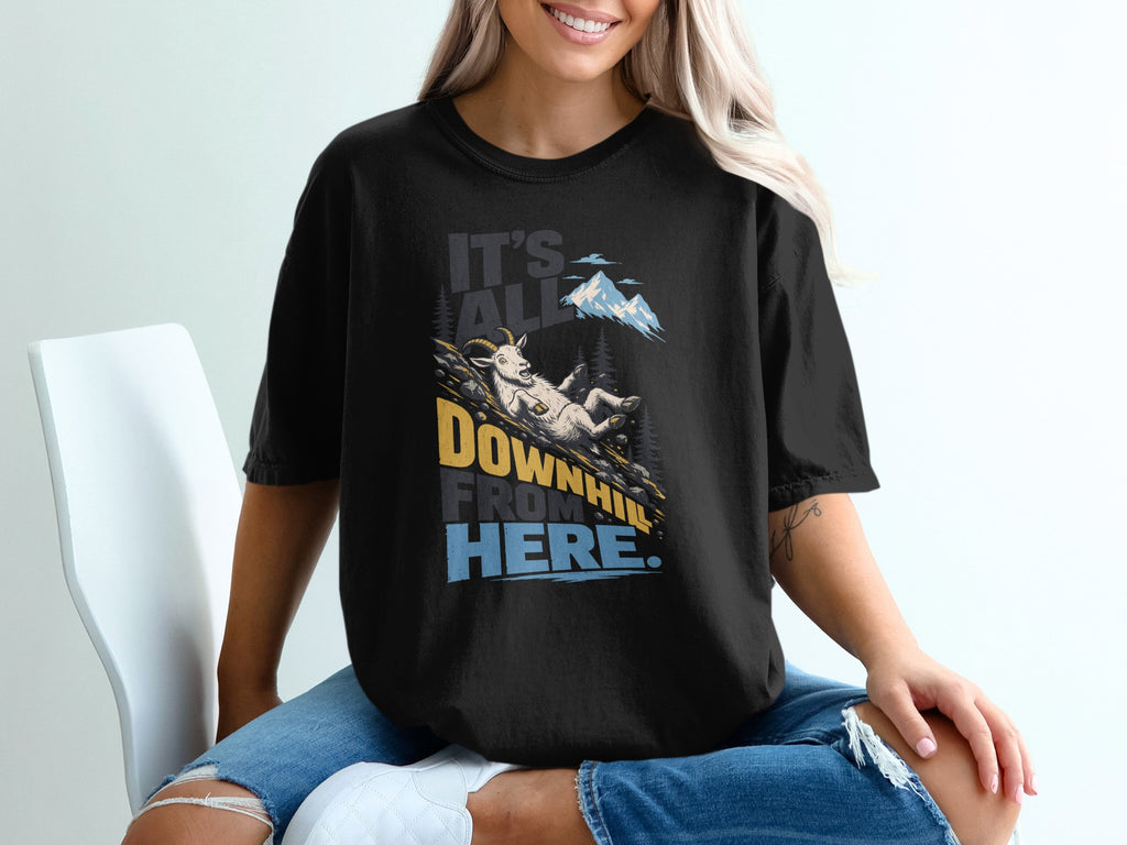 A person wearing a black t-shirt printed with a mountain goat sliding downhill and the text It's All Downhill From Here.