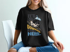 A person wearing a black t-shirt printed with a mountain goat sliding downhill and the text It's All Downhill From Here.