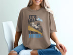 A person wearing a brown t-shirt featuring a mountain graphic and the text It's All Downhill From Here.