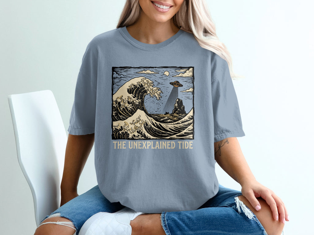 T-shirt graphic with a wave, UFO, and text "THE UNEXPLAINED TIDE".