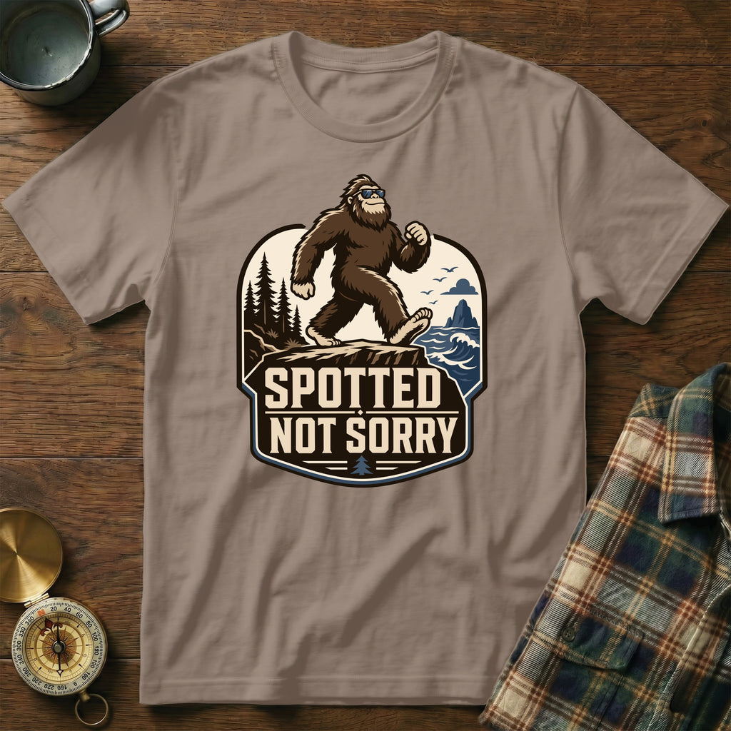 Bigfoot wearing sunglasses on a cliff overlooks the ocean, with text "Spotted Not Sorry".