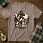 Bigfoot wearing sunglasses on a cliff overlooks the ocean, with text "Spotted Not Sorry".