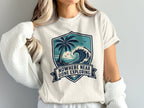T-shirt with ocean wave, palm tree and banner text "NOWHERE NEAR DONE EXPLORING".