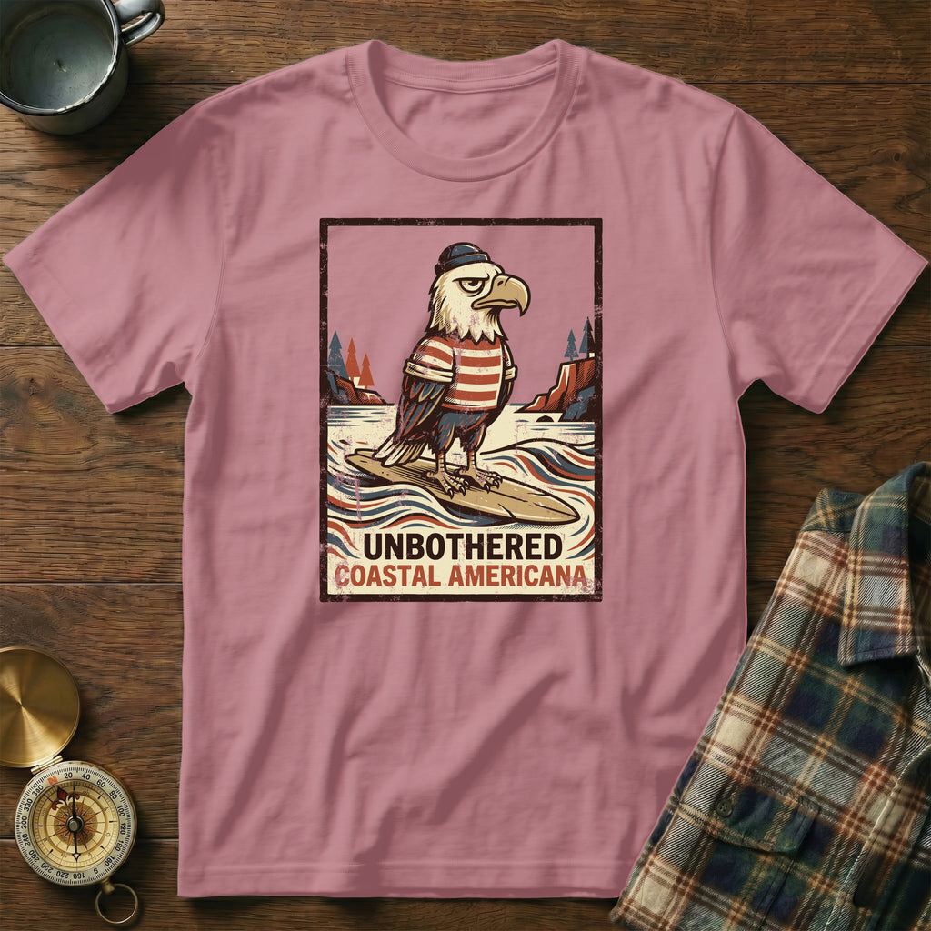 T-shirt with graphic of eagle in hat and striped shirt on surfboard, text "UNBOTHERED COASTAL AMERICANA".