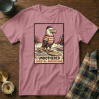 T-shirt with graphic of eagle in hat and striped shirt on surfboard, text "UNBOTHERED COASTAL AMERICANA".