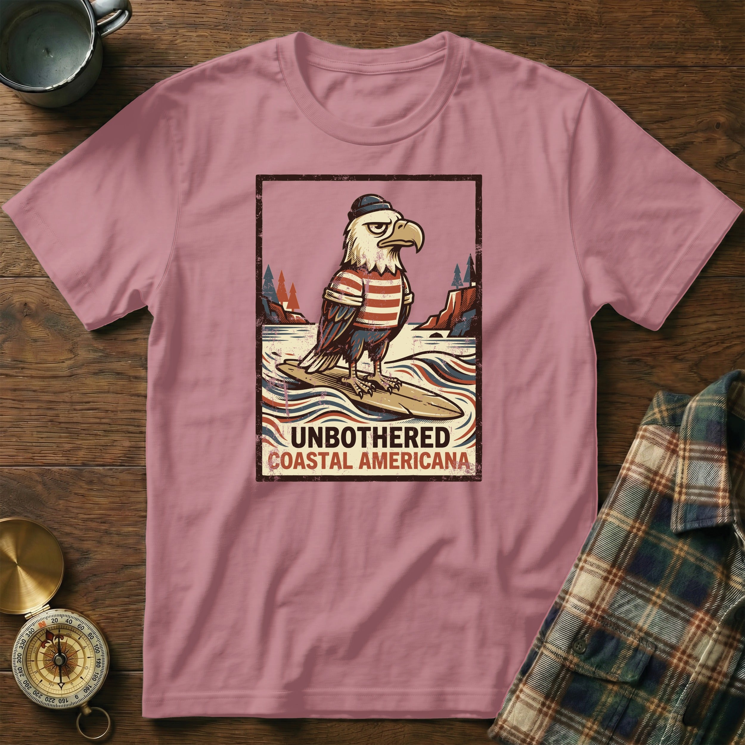 T-shirt with graphic of eagle in hat and striped shirt on surfboard, text "UNBOTHERED COASTAL AMERICANA".