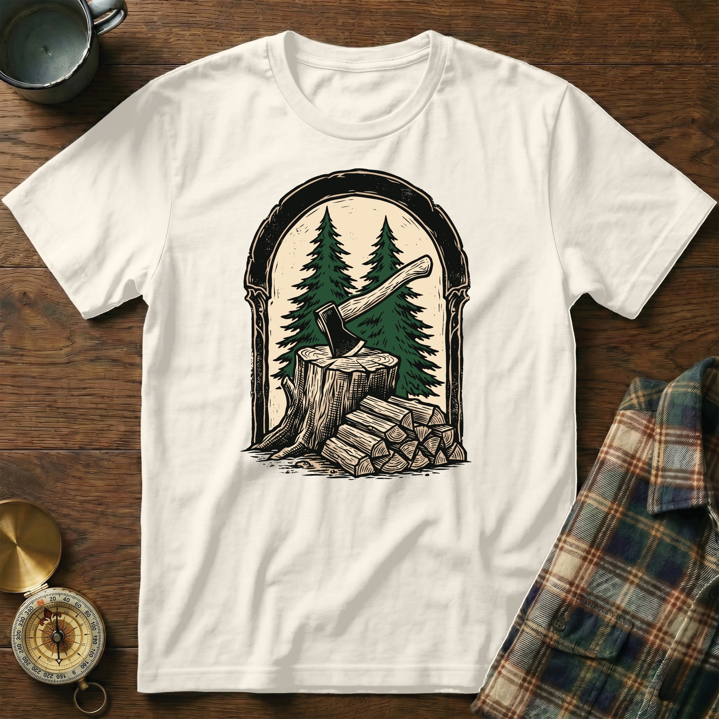 T-shirt with graphic of axe in tree stump with stacked firewood and evergreen trees.
