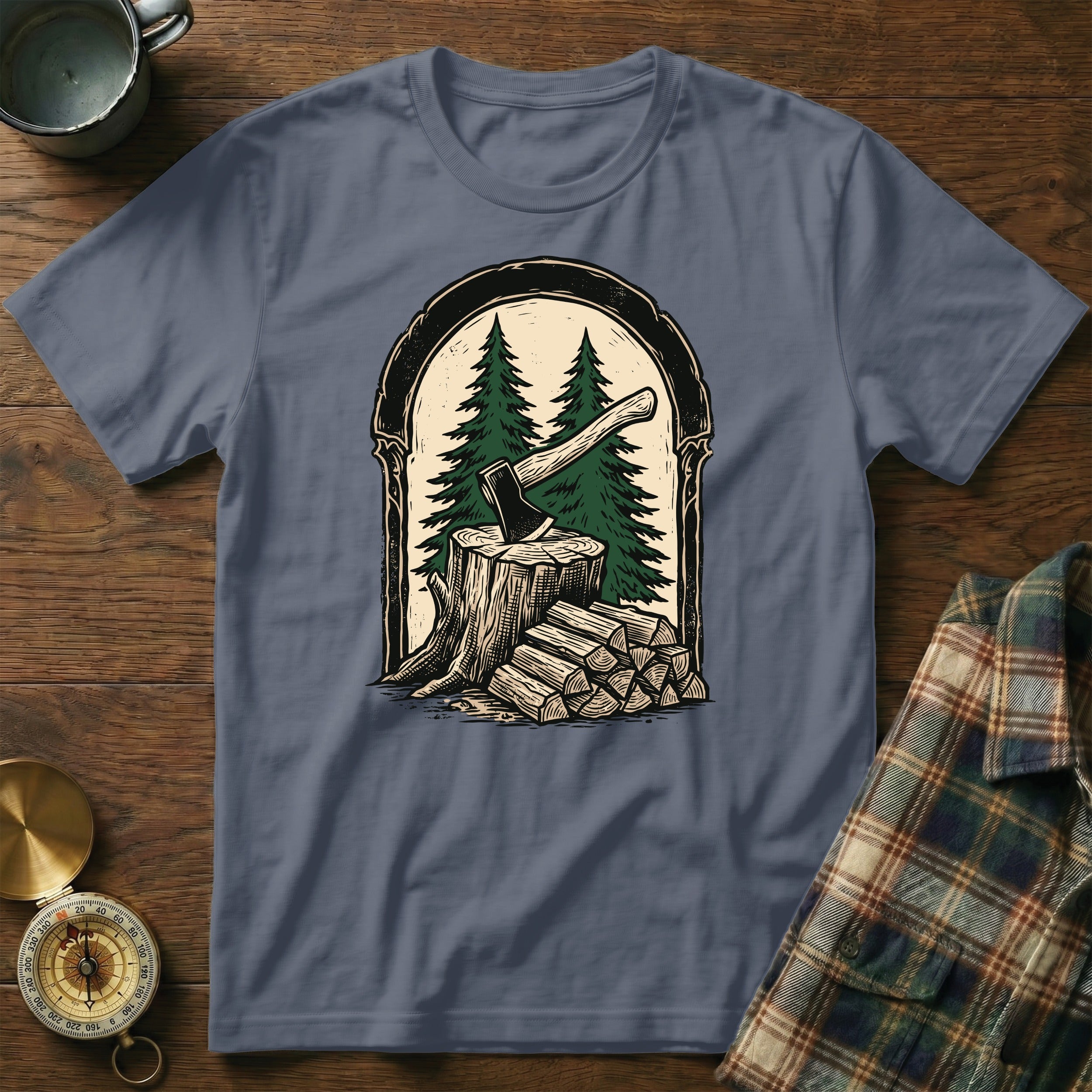T-shirt graphic of an axe in a tree stump with stacked firewood and pine trees.