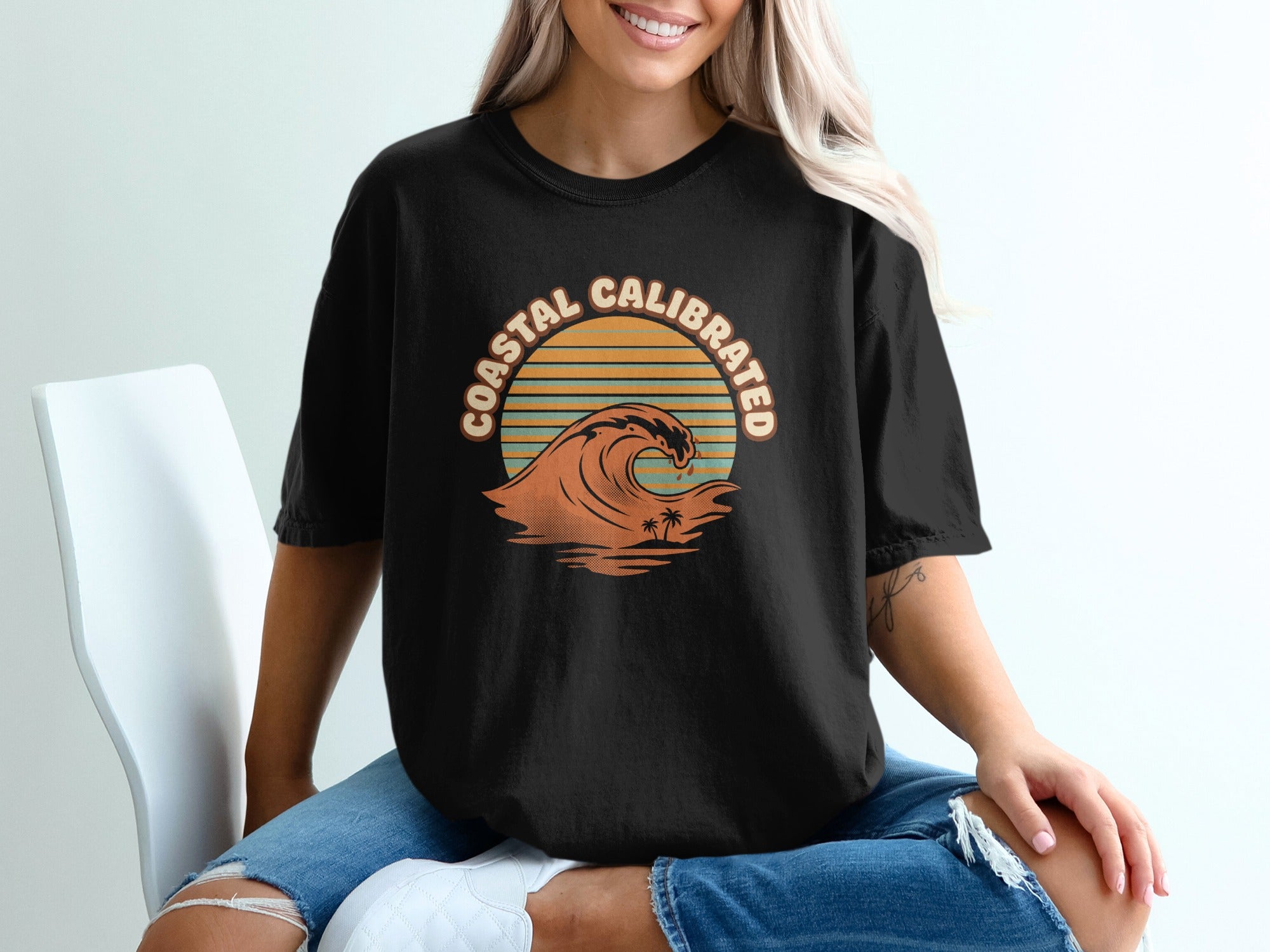 Black t-shirt with "COASTAL CALIBRATED" text and wavy sunset graphic.
