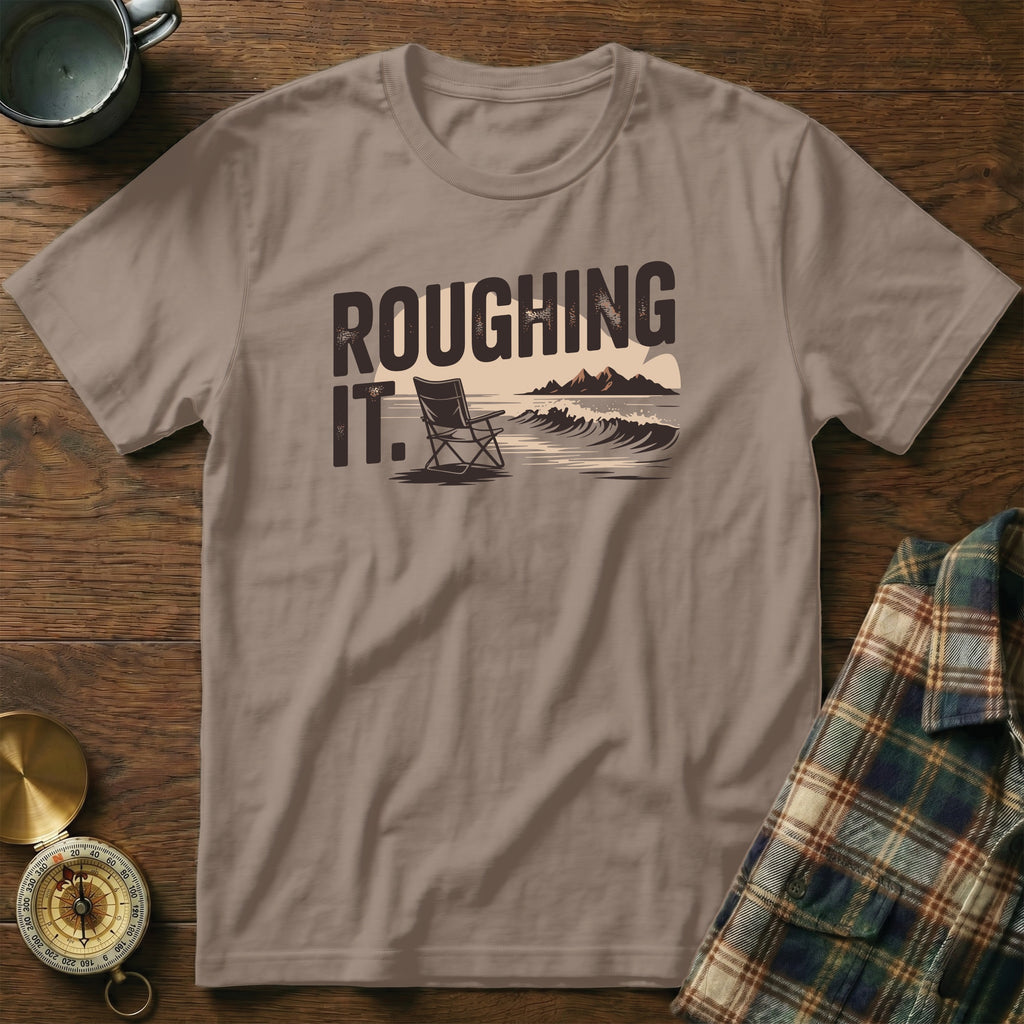 T-shirt with "ROUGHING IT." text, beach chair, ocean, and mountains.
