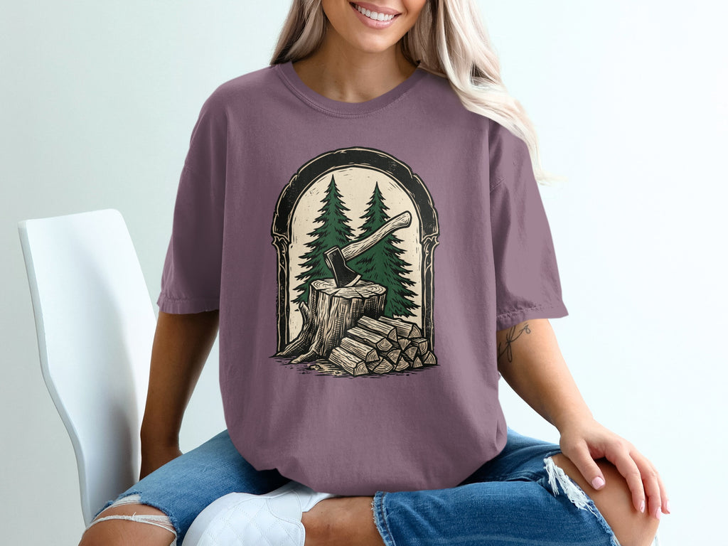 T-shirt graphic of axe in wood stump with pine trees and stacked wood.