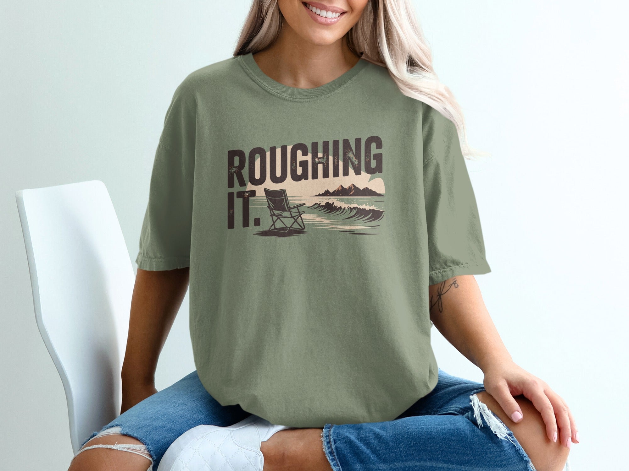 Olive green t-shirt with "ROUGHING IT." text and beach scene graphic.