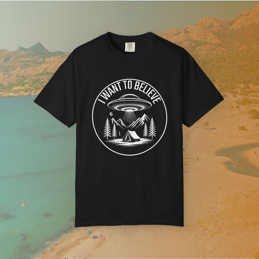  t-shirt A round, white graphic on a dark background featuring a classic flying saucer UFO abducting a tent at a campsite surrounded by mountains and pine trees. The surrounding text reads "I WANT TO BELIEVE.