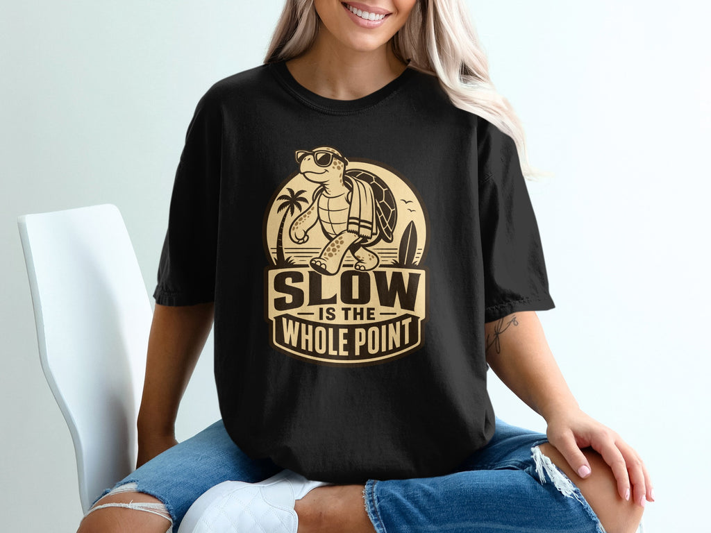 Black t-shirt with a graphic of a turtle on a tropical beach, saying "SLOW IS THE WHOLE POINT."