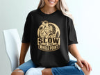 Black t-shirt with a graphic of a turtle on a tropical beach, saying "SLOW IS THE WHOLE POINT."