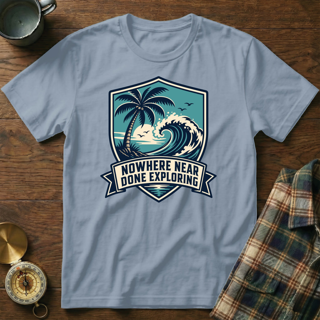 Light blue t-shirt with shield graphic featuring palm tree, wave, and text "Nowhere Near Done Exploring".