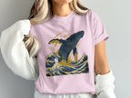 Pink t-shirt featuring a stylized whale breaching in dark blue and gold waves.
