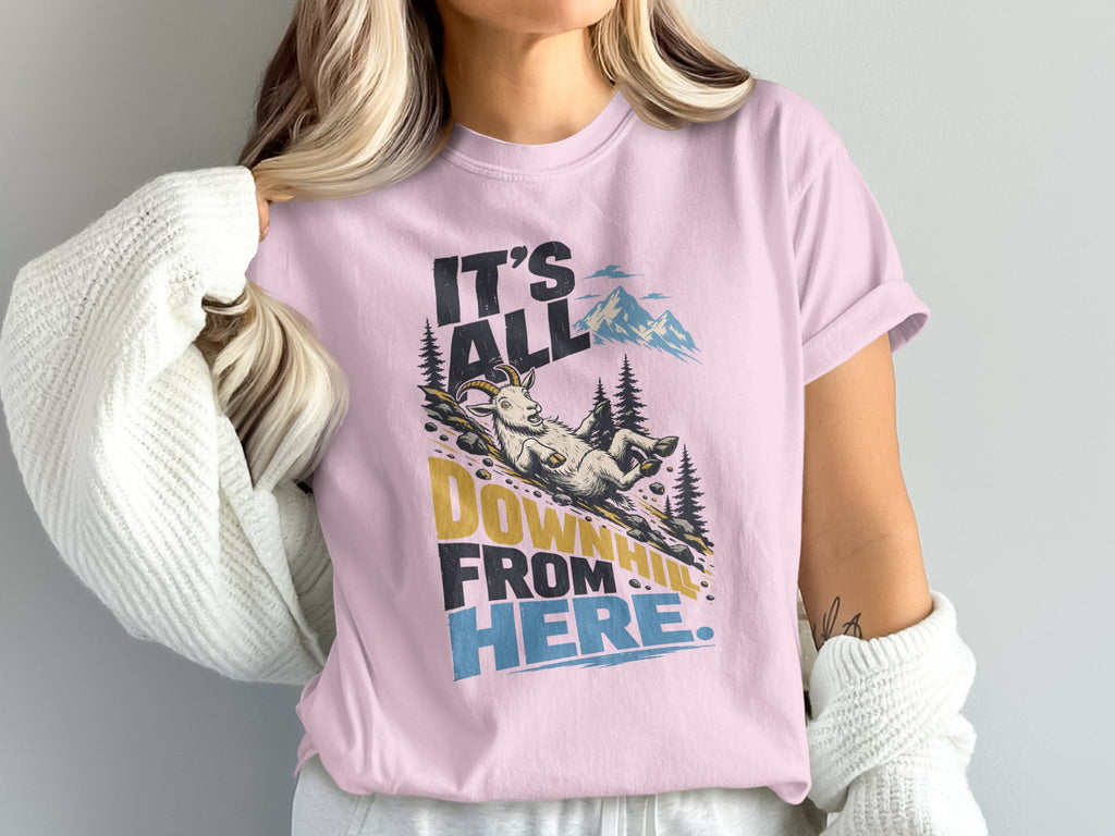 A light pink t-shirt worn by a person features the text It's All Downhill From Here and a graphic of a mountain goat sliding down a hill.