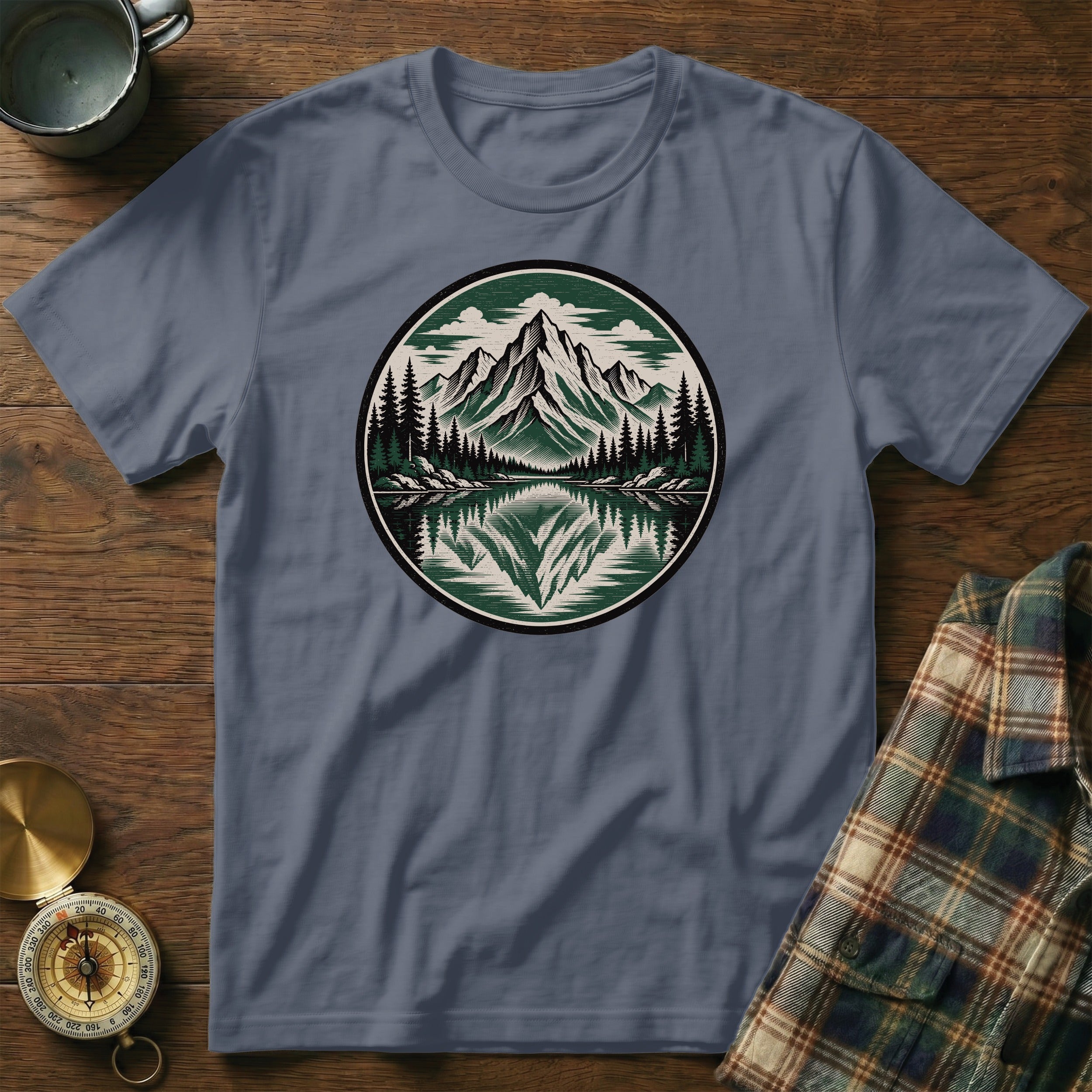 Blue t-shirt with circular mountain, lake, and forest graphic design.