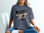 Dark gray t-shirt with "WILDERNESS EXPERT" text and beach scene graphic.
