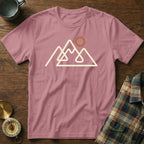 Pink t-shirt with a cream line drawing of mountains and a sun graphic.