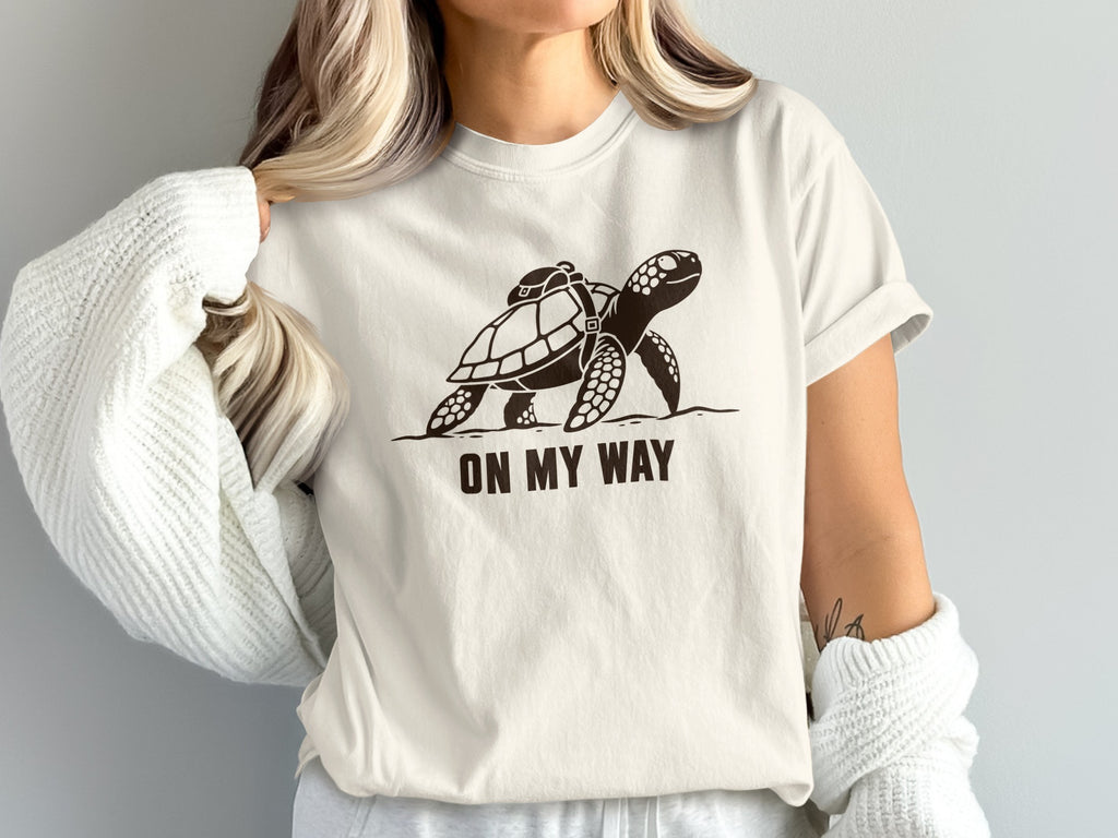 T-shirt with a dark brown graphic of a turtle wearing a backpack and the text "ON MY WAY."