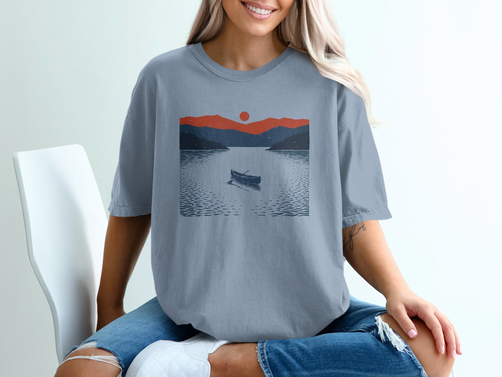 T-shirt with graphic of a canoe on a lake with mountains and a sunset.