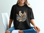 Black t-shirt with a graphic of an eagle surfing on a wave near a lighthouse.