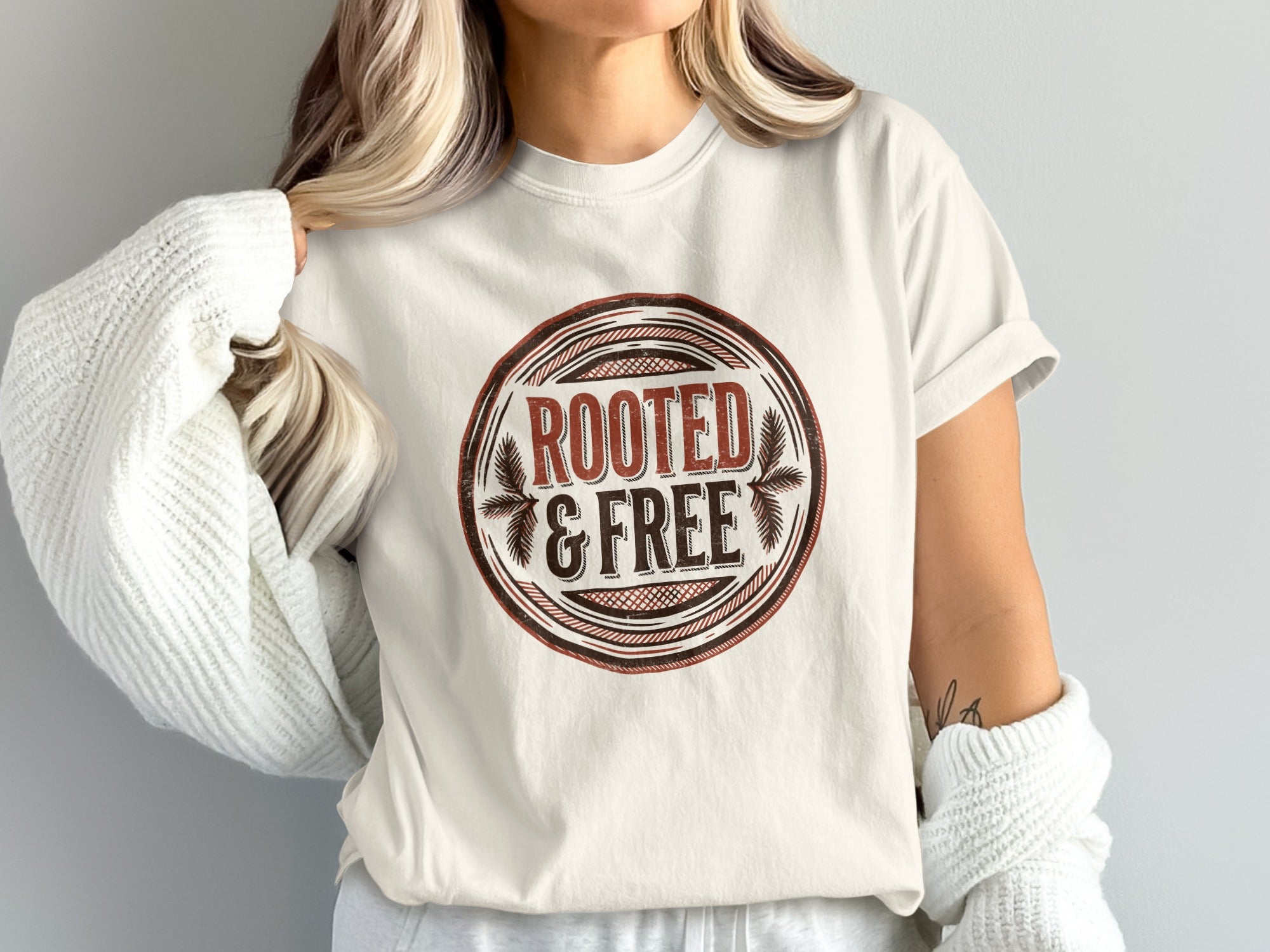 Cream t-shirt featuring a circular emblem with "ROOTED & FREE" text.