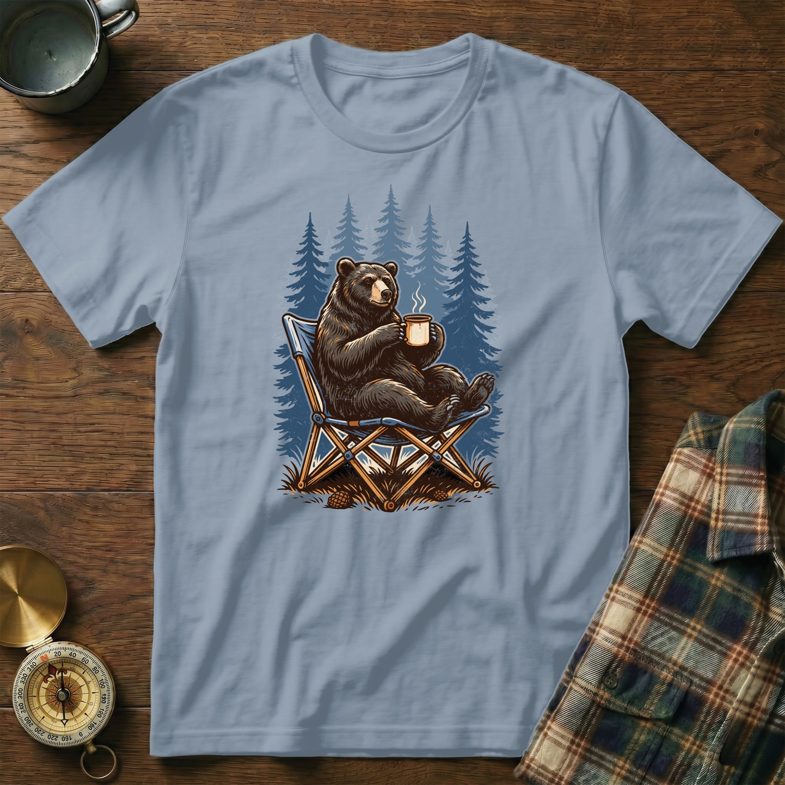 Bear in camping chair holding a mug in front of pine trees.