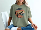 Green t-shirt with a retro desert landscape graphic featuring a cactus and mountains.