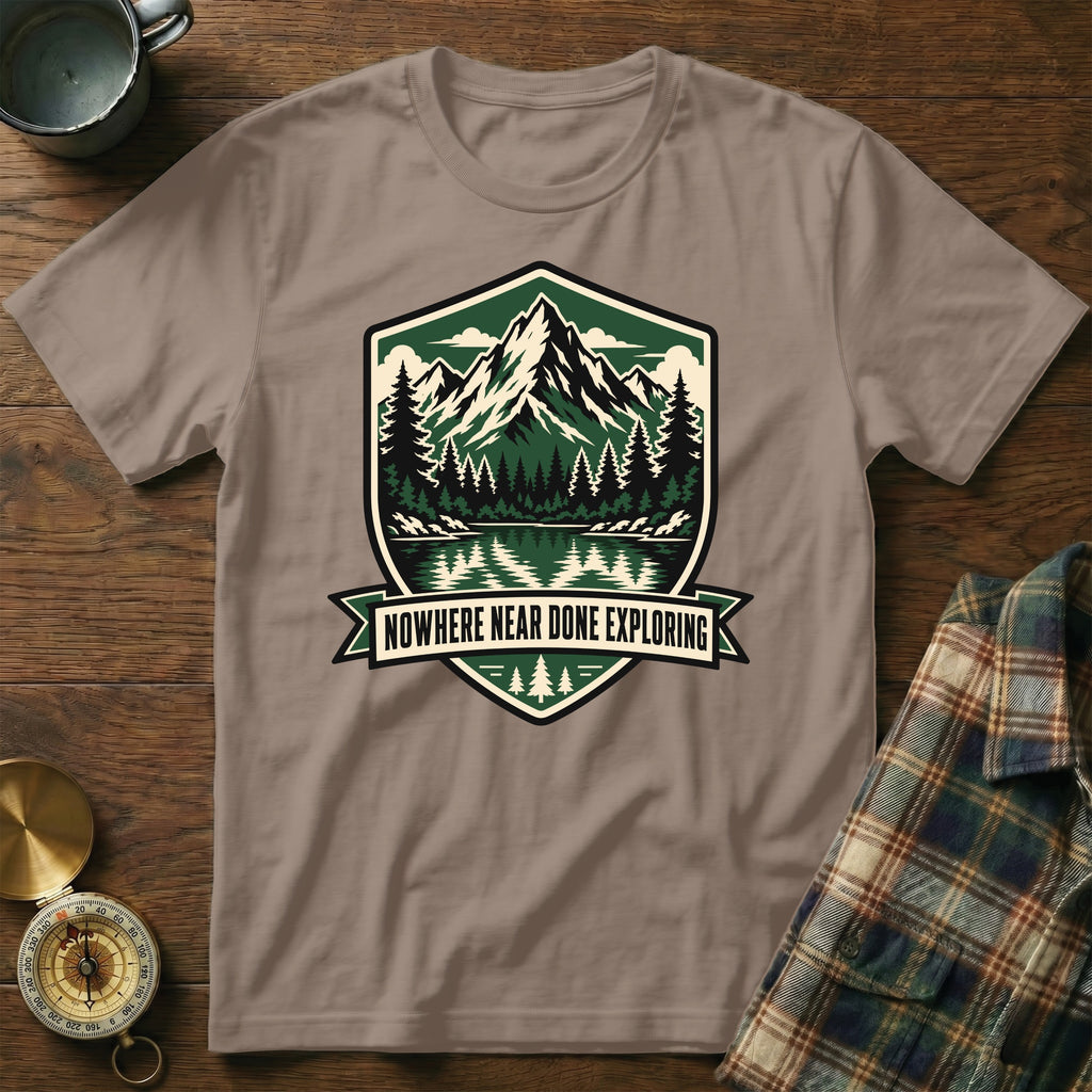 T-shirt with shield graphic of mountains, forest, and lake with text "NOWHERE NEAR DONE EXPLORING".