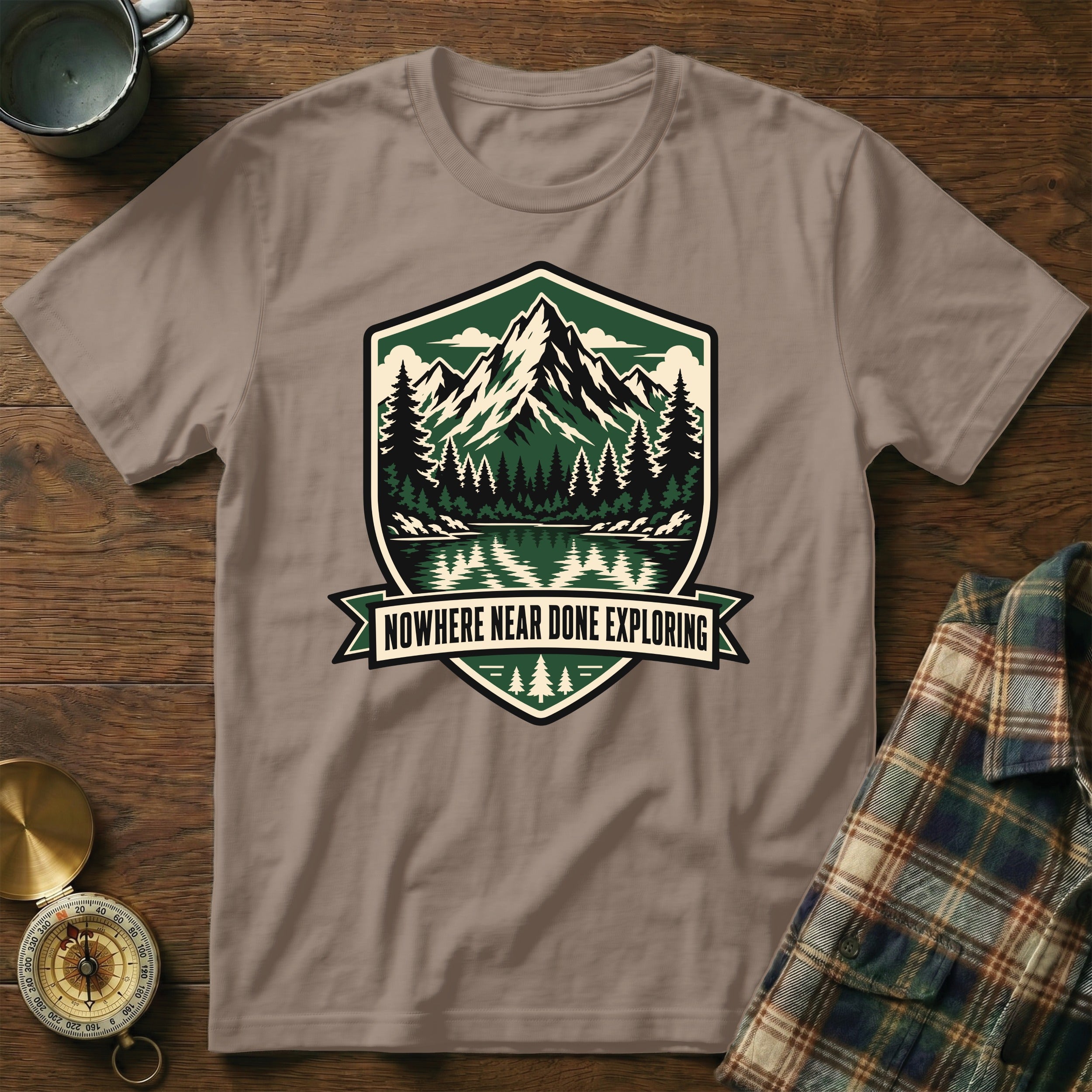 T-shirt with shield graphic of mountains, forest, and lake with text "NOWHERE NEAR DONE EXPLORING".
