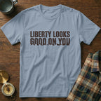 Light blue t-shirt with brown text "LIBERTY LOOKS GOOD ON YOU" and mountain graphic.